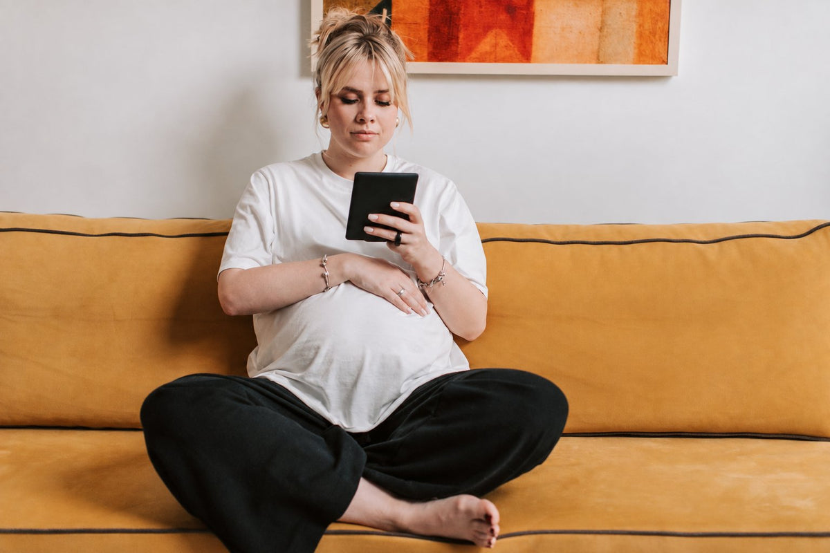Pregnant woman reading a tablet while relaxing on a sofa.
